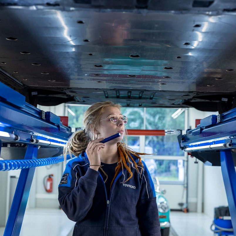 Eine TÜV NORD Expertin untersucht den Unterboden eines Autos auf einer Hebebühne mit einer Taschenlampe während eines AutoKaufChecks.