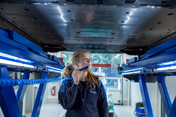 AutoKaufCheck Eine TÜV NORD Expertin untersucht den Unterboden eines Autos auf einer Hebebühne mit einer Taschenlampe während eines AutoKaufChecks.