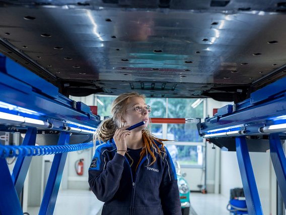 Eine TÜV NORD Expertin untersucht den Unterboden eines Autos auf einer Hebebühne mit einer Taschenlampe während eines AutoKaufChecks.