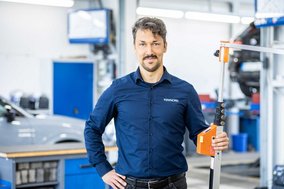 TÜV NORD Mitarbeiter mit Messgerät in einer Werkstatt, im Hintergrund Werkstattausrüstung und ein Auto.