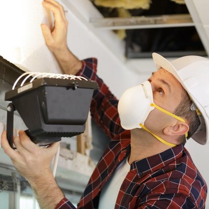 Deckenpruefung Mitarbeiter mit Atemschutzmaske und Sicherheitshelm begutachtet die Decke nach Schadstoffen.