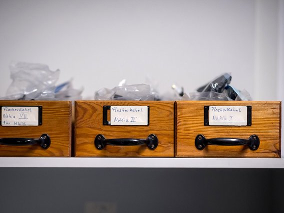 Holzschubladen mit Beschriftungen für "Flasher Kabel Nokia I, II und VII", die Gerätekomponenten enthalten.