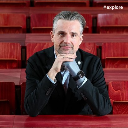 Bertolt Meyer in Anzug sitzt in einem Auditorium mit roten Sitzen und stützt nachdenklich seinen Kopf auf die Hand.
