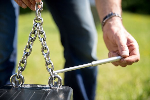 Nahaufnahme von Händen, die eine Metallkette halten. Eine Hand hält einen weißen Maßstab an die Kette, während die andere die Kette festhält.