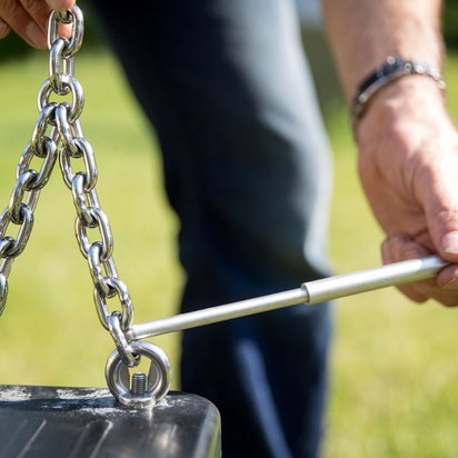 Nahaufnahme von Händen, die eine Metallkette halten. Eine Hand hält einen weißen Maßstab an die Kette, während die andere die Kette festhält.