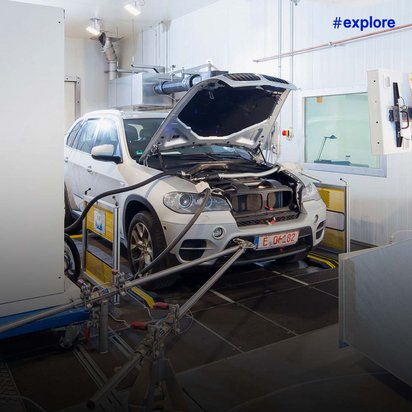 Weißer BMW SUV mit geöffneter Motorhaube auf einem Rollenprüfstand in einer modernen Kfz-Werkstatt mit blauer Hebebühne.