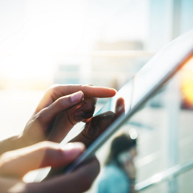 Nahaufnahme einer Hand, die auf einem Tablet tippt, mit unscharfem Hintergrund und Sonnenlicht