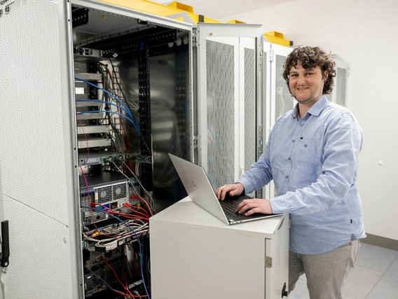 Ein IT-Techniker mit lockigem Haar arbeitet an einem Laptop vor geöffneten Serverschränken in einem Rechenzentrum.