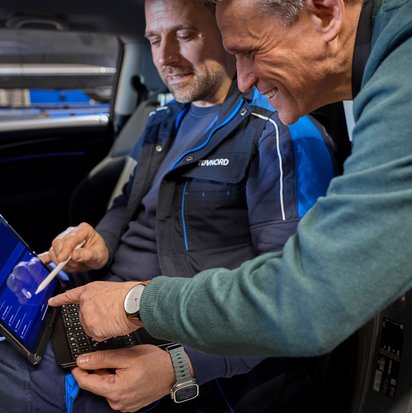 Prüfingenieur und Kunde bei der Fahrzeugprüfung mit Laptop