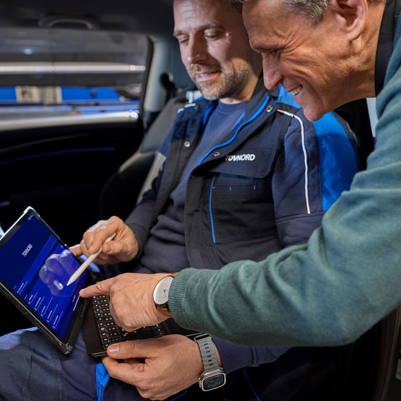 So funktioniert die digitale Fahrzeugdiagnose über OBD-Schnittstelle Zwei Männer im Auto mit einem Tablet in der Hand