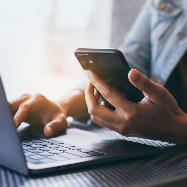 Person mit Smartphone und Laptop füllt ein Kontaktformular aus