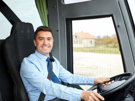 Ein Mann sitzt am Lenkrad eines Busses und lächelt.
