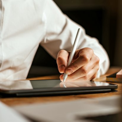 Person interagiert mit einem digitalen Dokument auf einem Laptop, während sie ein Smartphone hält.
