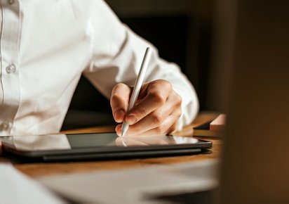 Person interagiert mit einem digitalen Dokument auf einem Laptop, während sie ein Smartphone hält.