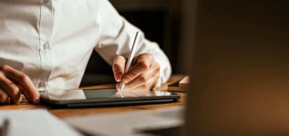 Person interagiert mit einem digitalen Dokument auf einem Laptop, während sie ein Smartphone hält.