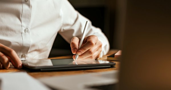 Person interagiert mit einem digitalen Dokument auf einem Laptop, während sie ein Smartphone hält.