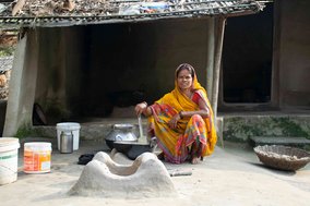 A woman is cooking over a modern fire pit which can be inspected in accordance with A 6.4.