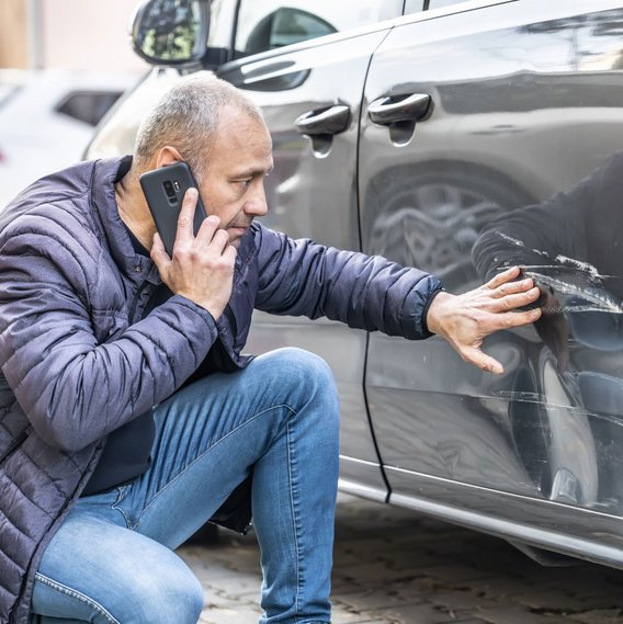 Mann sitzt am Auto mit Kratzern