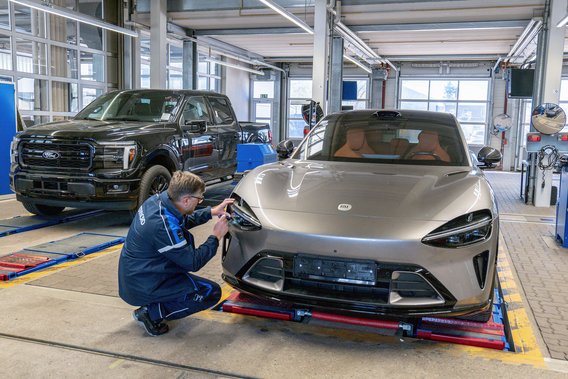 Einzelgenehmigung für Importfahrzeuge – TÜV NORD Prüfung von Scheinwerfern und Fahrzeugtechnik TÜV NORD Prüfer kontrolliert den Scheinwerfer eines importierten Sportwagens im Rahmen der Einzelgenehmigung, im Hintergrund ein Pick-up-Fahrzeug auf dem Prüfstand.