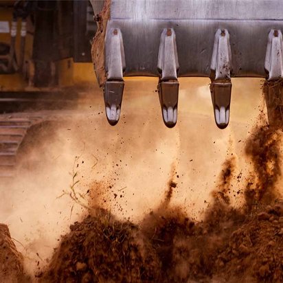 Nahaufnahme eines Baggers, der Erde bewegt, mit Fokus auf die Schaufel und die Ketten. Description: Das TÜV NORD Schulungszentrum bie