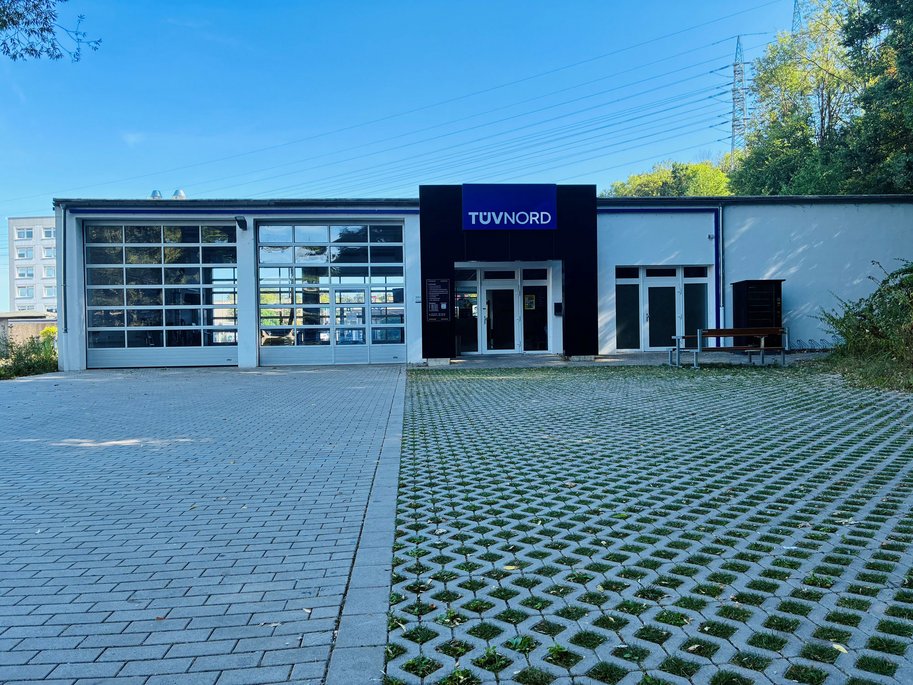 TÜV NORD Station – Außenansicht Außenansicht einer TÜV NORD Station mit Glasgaragentoren, Eingangsbereich und großem Vorplatz.