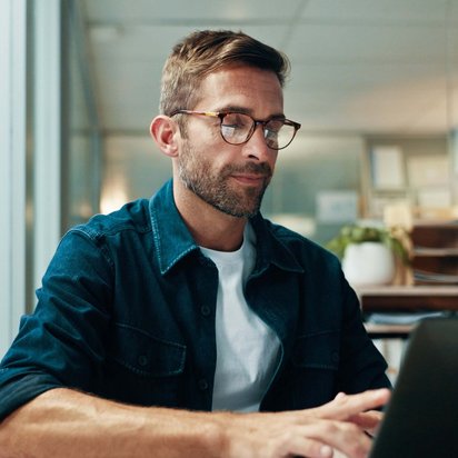 Mann sitzt am Laptop und schreibt einen Artikel über Künstliche Intelligenz (KI) für den TÜV NORD Blog für berufliche Weiterbildung.