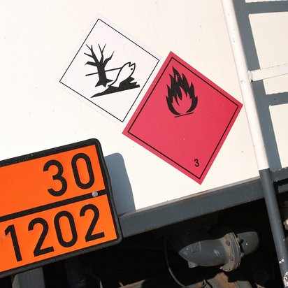 Gefahrgutkennzeichnung auf einem Transportfahrzeug mit Symbolen für Umweltgefahr und entzündbare Flüssigkeiten.