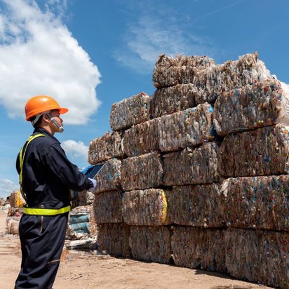 An officer in safety clothing stands next to a pile of rubbish with a tablet in his hands.