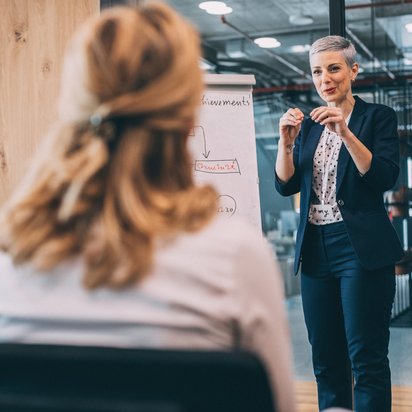 Frau hält Präsentation vor Kollegin mit Flipchart in modernem Büro