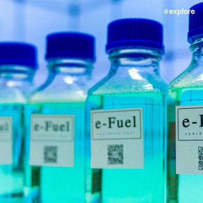Eine Reihe von durchsichtigen Flaschen mit türkisfarbener Flüssigkeit und blauen Verschlüssen. Die Etiketten zeigen "e-Fuel" und QR-Codes. Es handelt sich um synthetischen Kraftstoff in einem Labor.