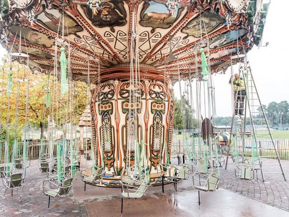 Ein traditionelles Kettenkarussell mit kunstvoll verzierter Mitte und leeren Sitzen, aufgestellt auf gepflastertem Boden in einem Freizeitpark im Herbst.