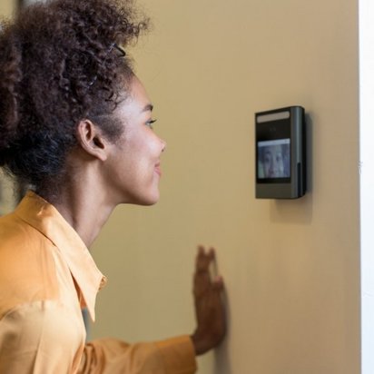 Eine Frau mit lockigem Haar in orangefarbener Bluse nutzt ein Zugangskontrollsystem. Ihr Profil ist zu sehen, während sie vor einem Wanddisplay steht.