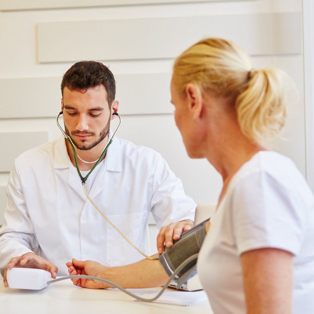 Ein Arzt misst den Blutdruck einer Patientin während einer arbeitsmedizinischen Untersuchung.
