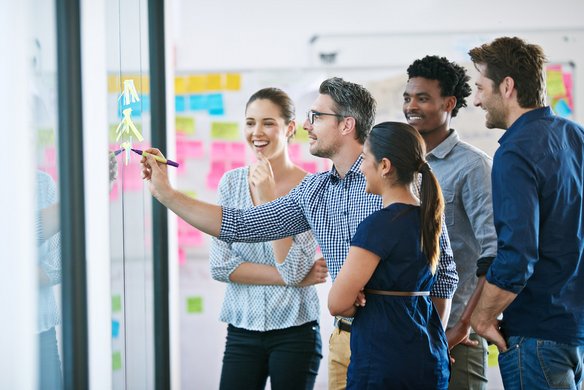 Team steht vor einem Whiteboard und entwickelt gemeinsam kreative Ideen.