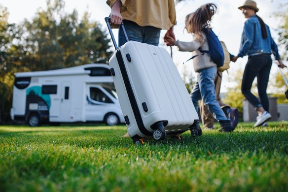 Familie mit Gepäck vor einem Wohnmobil auf einer Wiese