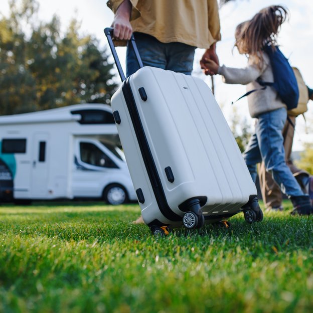 Familie mit Gepäck vor einem Wohnmobil auf einer Wiese