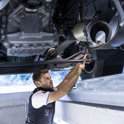 Prüfingenieur arbeitet am Unterboden eines Fahrzeugs an einer TÜV NORD Station
