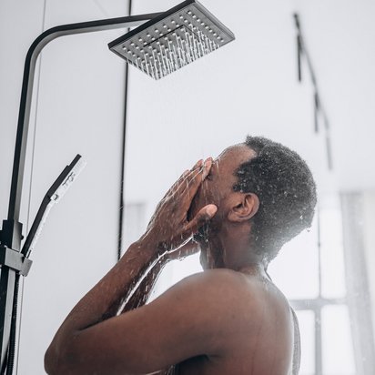 TÜV NORD_Trinkwasser_Hygiene_Dusche Junger Mann steht unter einer modernen Dusche