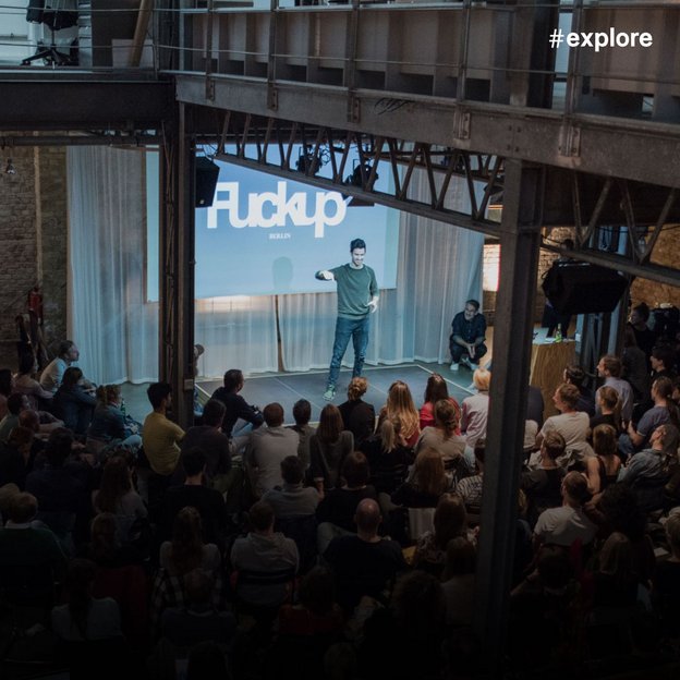 Eine Veranstaltung mit "Fuckup" im Hintergrund projiziert, bei der eine Person auf der Bühne vor einem großen Publikum steht.