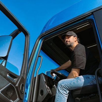 Lkw-Fahrer mit Basecap sitzt in einem blauen Lkw und blickt aus der geöffneten Tür