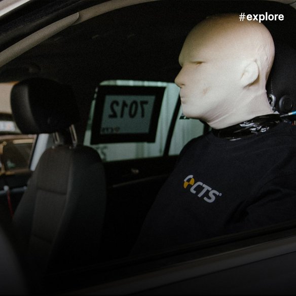 Crashtest-Dummy sitzt auf dem Fahrersitz eines Testfahrzeugs, ausgestattet mit Messinstrumenten.