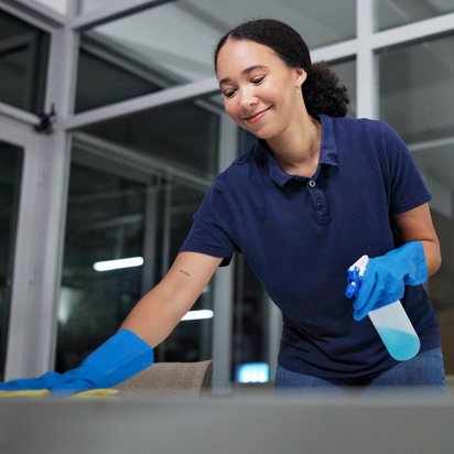 TÜV Nord Gefahrstoffe – Sicherheit am Arbeitsplatz Reinigungskraft beim Wischen eines Tisches in einem modernen Büro