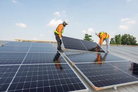 Zwei Arbeiter montieren Solarpanels auf einem Dach bei sonnigem Wetter.