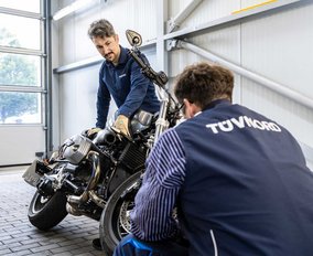  Zwei TÜV NORD Mitarbeiter prüfen gemeinsam ein Motorrad in einer modernen Werkstatt.