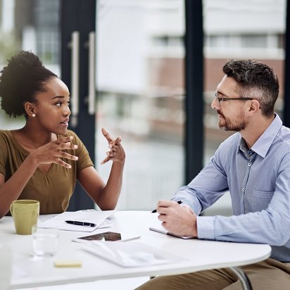 Altersmanagement für gesunde und produktive Arbeitskräfte bei Medituev Zwei Personen führen ein Gespräch am Tisch, während sie sich gestikulieren und Notizen machen