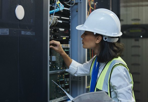 Technikerin mit Helm prüft Serverkomponenten in einem Rechenzentrum.