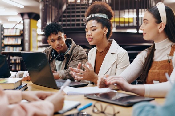 Gruppe junger Menschen arbeitet gemeinsam mit Laptops und Notizen in einer Bibliothek