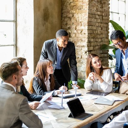 Gruppe von Geschäftsleuten diskutiert lebhaft in einem modernen Besprechungsraum mit Industrie-Charakter.