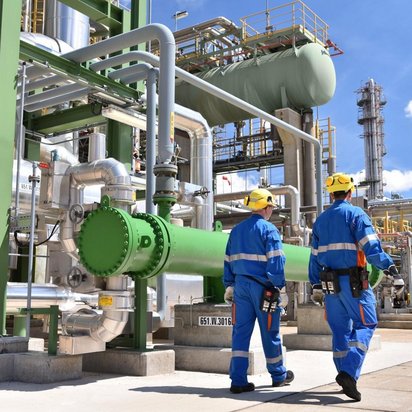 Anlagen- und Systemtechnik für Industrie und Infrastruktur Industrieanlage mit Rohrleitungen und verfahrenstechnischen Systemen. Zwei Fachkräfte führen eine Anlagenbegehung zur Bewertung von Sicherheit, Funktion und Betriebszustand durch.