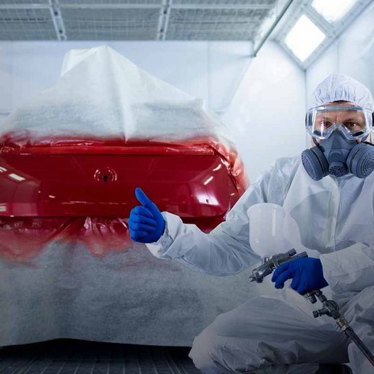 Fahrzeuglackierer in Schutzkleidung bei der Arbeit in einer Lackierkabine, rotes Auto wird lackiert